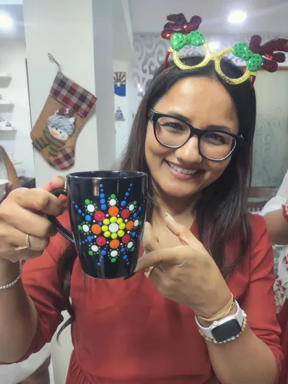 A guest at a Christmas-themed art party shows off her festive and intricate dot mandala mug. Themed parties are a fantastic way to celebrate holidays and create unique seasonal keepsakes.