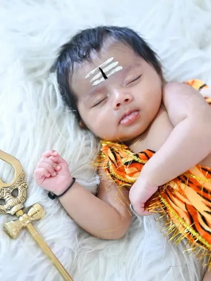 A newborn Bala Shiva, sleeping peacefully on a white fur blanket with a Trishul prop.