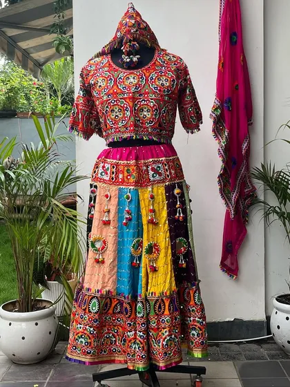 A beautiful women's chaniya choli with a multi-colored panel skirt and a bright pink dupatta. The intricate embroidery on the blouse is a highlight.