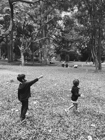 A black and white photo of children chasing giant bubbles in the park. This captures a timeless moment of childhood joy, a frequent sight at Cubbon Tales.