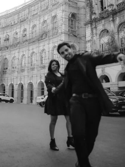 A playful, candid moment captured in black and white. His spontaneous movement towards the camera adds a sense of fun and authenticity to their urban photoshoot.