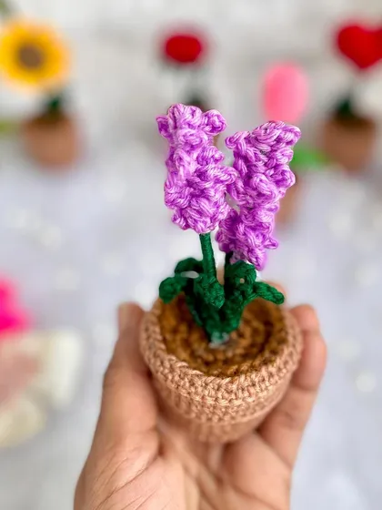 Holding a tiny pot of crochet lavender. The texture and color are designed to look just like the real thing, but it lasts forever.