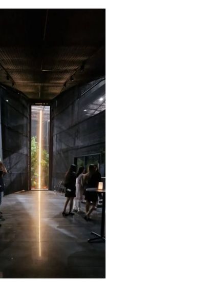 The interior of the Durall Pavilion, where a vertical line of light acts as a focal point. The dark, mesh clad space creates a dramatic atmosphere for showcasing products and hosting events.