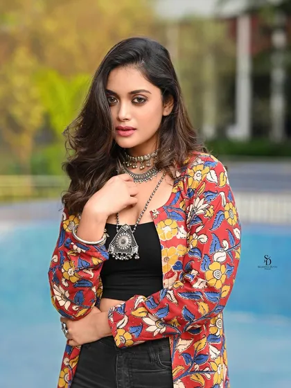A model poses by a pool in a modern, bohemian-chic outfit. The combination of a floral jacket, crop top, and layered necklaces is perfect for a summer festival look.