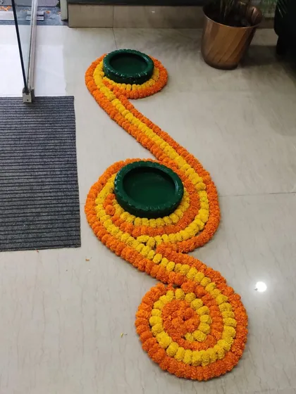 A simple yet elegant floor decoration for an entryway. I used yellow and orange marigold strings to create a winding pattern, with green matkas (earthen pots) placed as decorative accents.
