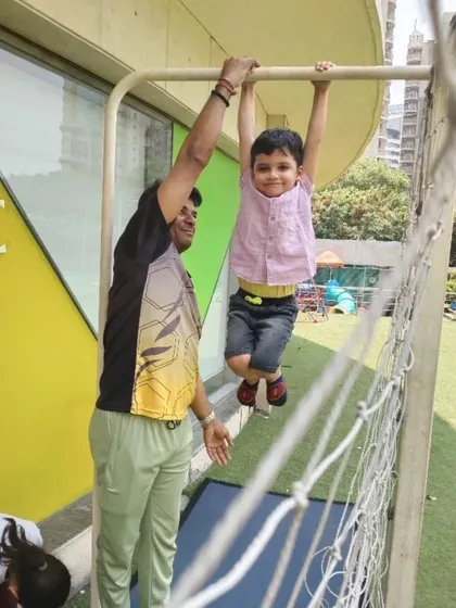 With a smile of accomplishment, a young student hangs from the bars with the help of a coach. These activities are crucial for building physical confidence and strength during our Summer Fungama.