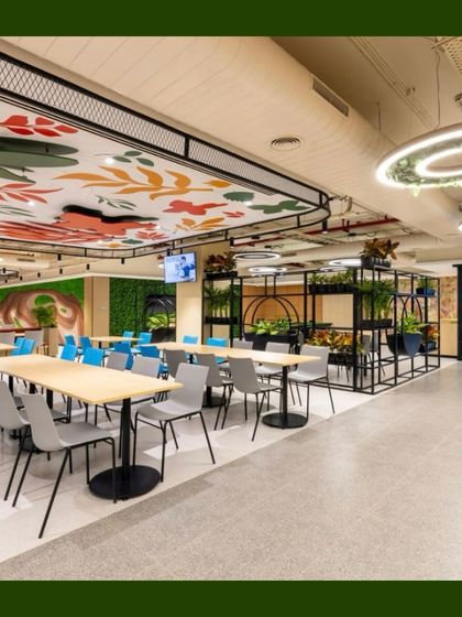 A wide shot of a corporate cafeteria we "green-ed up." The space features a mix of plant solutions, including planters, a green wall, and hanging greenery from the light fixtures, all working together to create a refreshing and inspiring place to eat and socialize.
