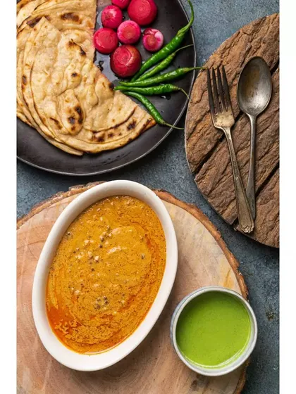 A rustic, top-down view of Dal Makhani with parathas and green chutney. The use of wooden textures and dark surfaces gives this shot a traditional and earthy feel.