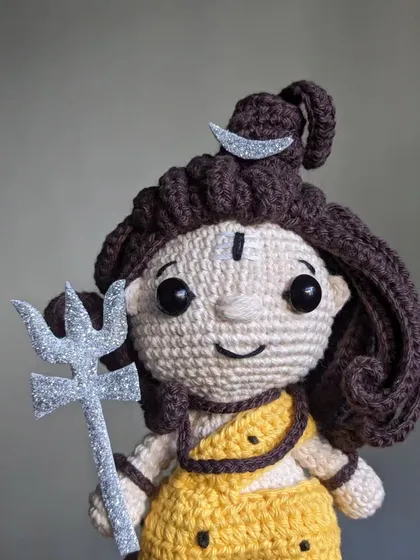 A close-up of the Lord Shiva doll, focusing on his calm face and the glittering Trishula.