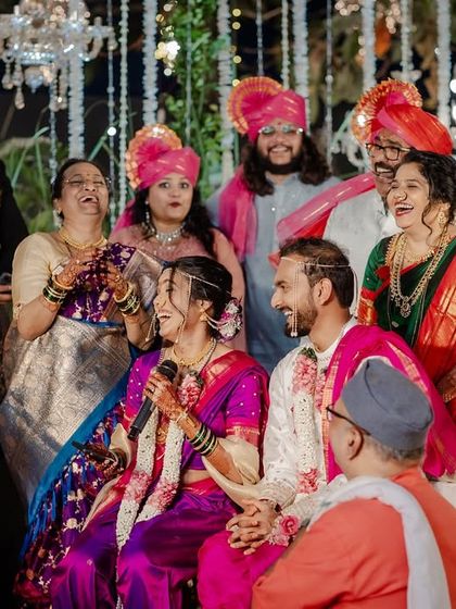 The 'ukhane' tradition in a Maharashtrian wedding, where the bride introduces her husband's name in a rhyming couplet, surrounded by laughing family.