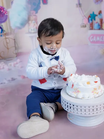 A full view of the cake smash scene, with the little one happily digging into his cake on a soft pink floor drop.