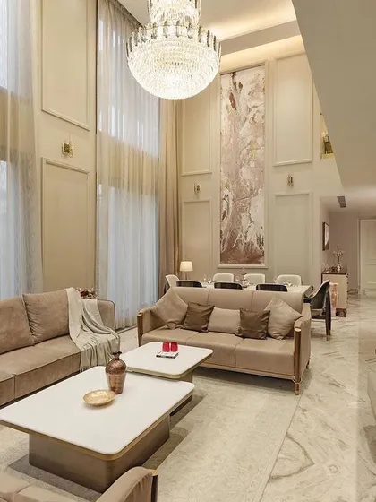 This double-height drawing room in our neoclassical project exudes opulence. The towering walls with classic molding, a grand crystal chandelier, and plush, neutral-toned furniture create a space that is both majestic and inviting.