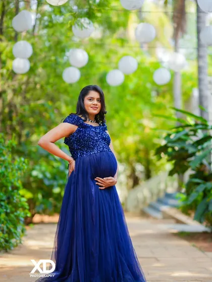 A graceful solo portrait of the mother-to-be in a sequined blue gown, surrounded by hanging lanterns.
