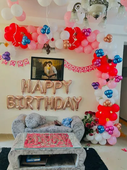 A colorful and lively birthday decoration in a living room, with a balloon garland framing a photo of the couple.