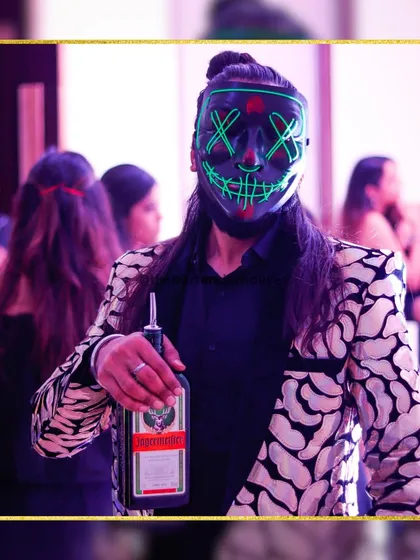 A masked marvel ready to serve. This look, combining a formal jacket with a neon mask, is perfect for a high-energy cocktail party or sangeet.