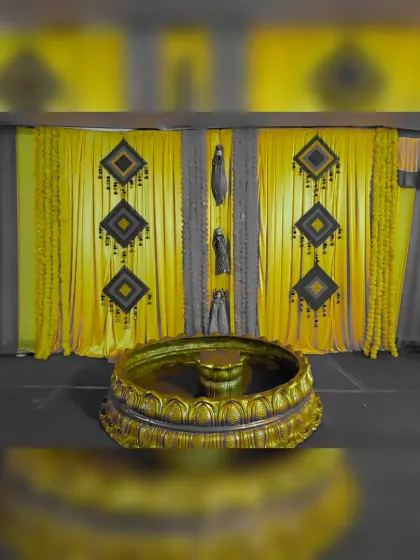 For a more contemporary Haldi theme, I used a striking color combination of yellow and grey. The backdrop features yellow drapes with geometric hangings, complemented by a large, ornate golden urli in the front.