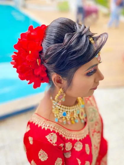 A modern take on a bridal bun, accented with a large, vibrant red floral piece. This hairstyle is perfect for brides who want a bold and contemporary touch to their wedding look.