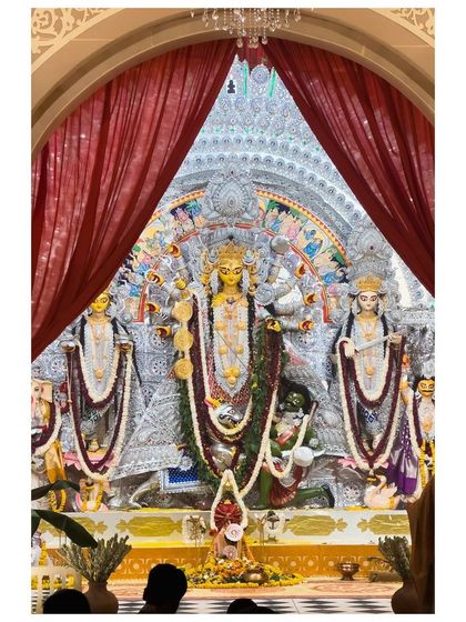 A magnificent silver-themed Durga idol, revealed through parted red curtains, creating a sense of theatrical grandeur.