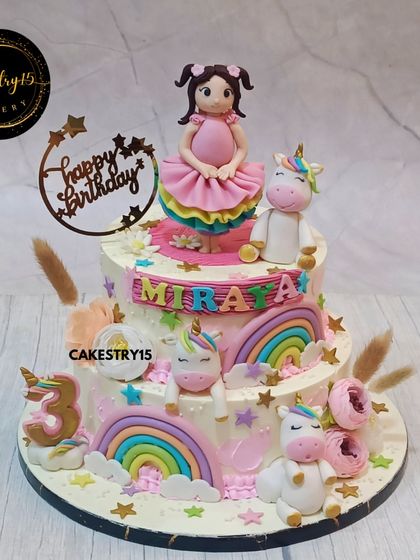 A magical two-tier unicorn cake for a third birthday. This chocolate cake features a doll topper, multiple fondant unicorns, rainbows, and stars, creating a truly enchanting birthday centerpiece.