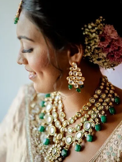 A detailed shot of the bride's soft makeup, elegant floral bun, and stunning emerald and polki jewelry. A perfect blend of tradition and grace.