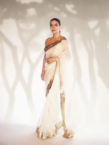 A full-length portrait showcasing the ethereal flow of the sheer white saree against a creatively lit backdrop.