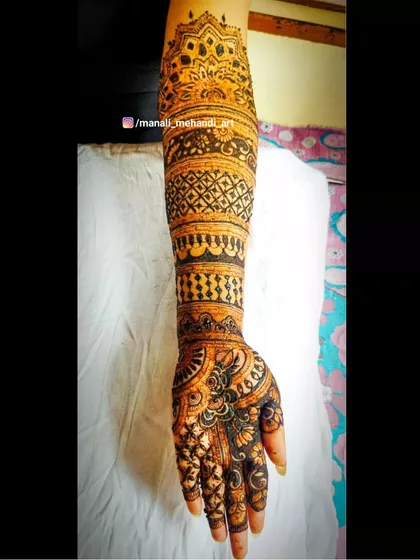 A single-arm view of a bridal mehandi, focusing on the intricate patterns. The design flows from a mandala at the top down through various bands of traditional line and dot work.