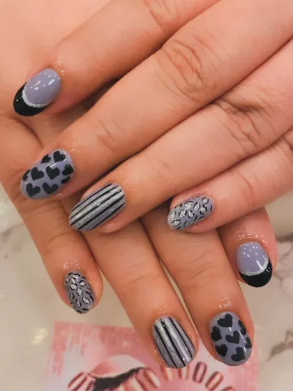 A playful mix-and-match set on short, natural nails. The design includes hand-painted hearts, stripes, and floral patterns in a grey, black, and white color scheme.