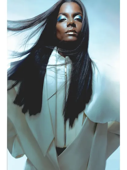 A close-up portrait with dramatic blue and gold makeup. The styling is clean and futuristic, with the focus on the model's intense gaze and the pop of metallic color.