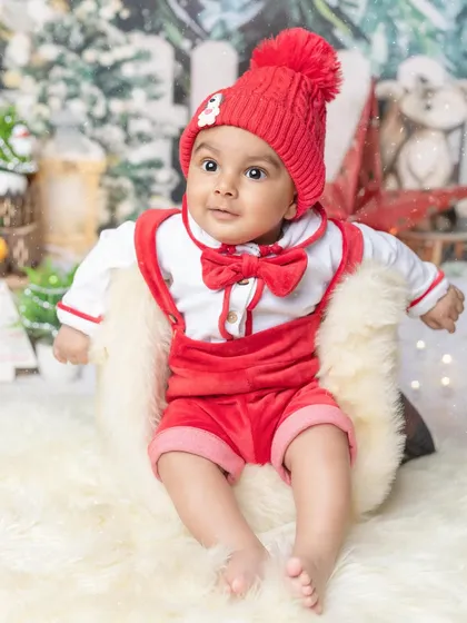 A curious little Santa sitting up in his chair. The winter wonderland backdrop and cozy red outfit create a magical holiday photo.