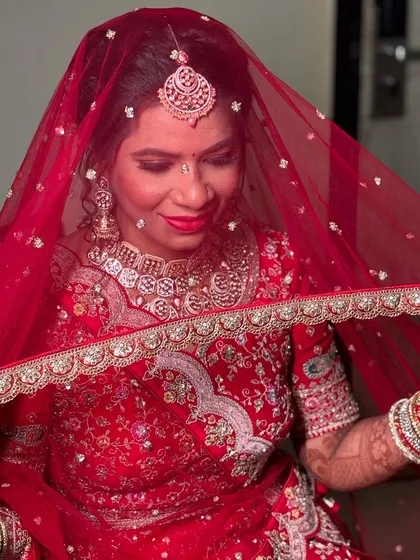 A classic bridal pose with the dupatta covering her head, her beautiful makeup shining through.