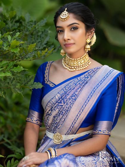 A royal blue Kanchivaram saree paired with a matching silk blouse. The blouse has a simple, elegant neckline, allowing the beauty of the silver-zari saree to take center stage.