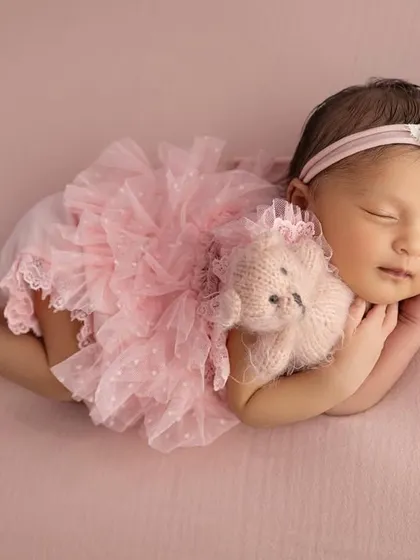 A baby girl in a frilly pink dress, cuddling a tiny teddy bear. This adds a sweet, playful element to a classic posed portrait.