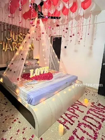 A modern first night setup with 'Just Married' balloons and a canopy. On the floor, I spelled out 'Happy Wedding' with rose petals and added flameless candles for a safe, romantic glow.
