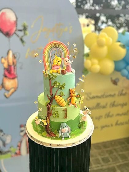 A beautiful Winnie the Pooh cake set against its party backdrop. The cake features a pastel rainbow and all the classic characters.