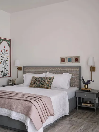 A serene bedroom with a custom headboard upholstered in a traditional block-print fabric, paired with antique art and a soft color palette.
