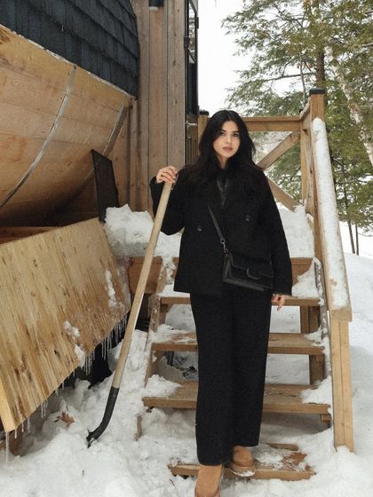 A winter wonderland scene from a cabin trip in Parry Sound. The all-black outfit contrasts with the snow, and the shovel adds a touch of authentic cabin life reality.