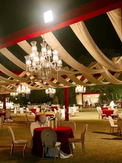 A wide view of the outdoor reception area, with a canopy of red and white drapes and numerous crystal chandeliers creating a grand and festive atmosphere.