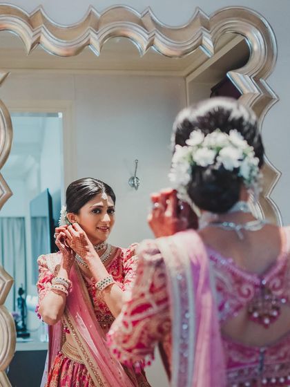 A beautiful moment of the bride getting ready. The reflection shows the intricate floral bun, which pairs perfectly with the soft, romantic makeup.