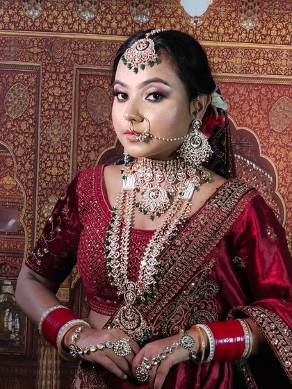 A bride in a deep red lehenga wearing a layered silver-toned jewellery set with green accents. This offers a unique alternative to traditional gold jewellery.