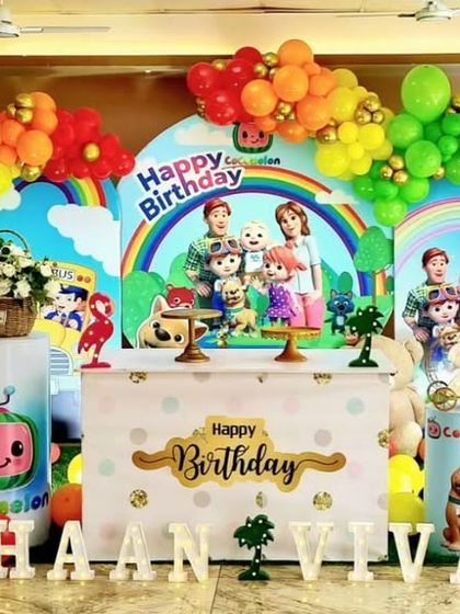 A vibrant and colorful Cocomelon themed birthday party. The setup is filled with characters from the show, a rainbow balloon arch, and custom name and age displays for a cheerful celebration.