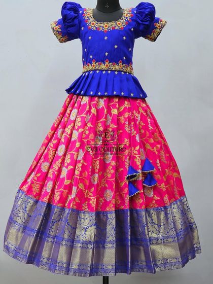 This royal blue and pink Banarasi lehenga is perfect for any celebration. The peplum blouse is embroidered, and the floral brocade skirt has a wide blue and gold zari border.