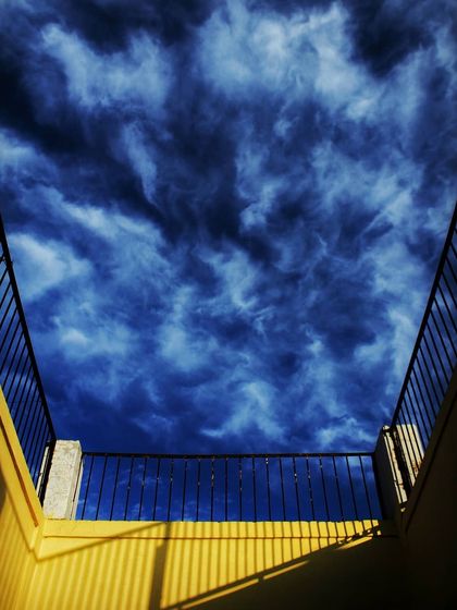 An empty balcony frames a beautiful, textured sky. The image is about the simple beauty of looking up and appreciating how the sun whispers goodbye in soft gold.