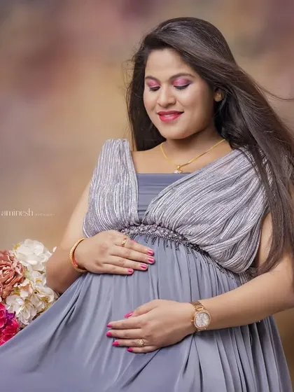 A simple and beautiful portrait in a grey Grecian-style gown. The focus here is on the mother's peaceful expression as she cradles her bump, with soft floral accents nearby.