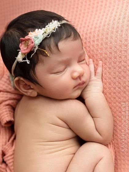 A newborn girl in a side-lying pose, wearing a floral headband. This classic pose is perfect for showcasing the baby's delicate profile and curled-up form.
