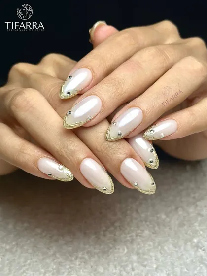Elegance in its purest form. This set features long almond extensions with a pearlescent white finish, accented with a delicate gold chrome border and minimalist silver rhinestone details for a sophisticated look.