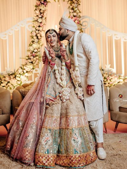 A joyful and candid moment where the groom gives his bride a happy kiss on the cheek, surrounded by beautiful floral decor.