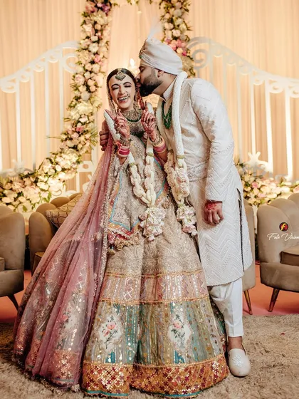 A joyful and candid moment where the groom gives his bride a happy kiss on the cheek, surrounded by beautiful floral decor.