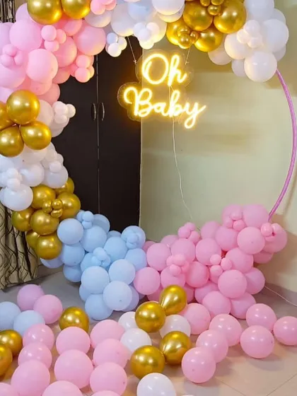 A modern baby shower setup with a pink, blue, white, and gold balloon ring. The 'Oh Baby' neon sign adds a trendy touch to the celebration.