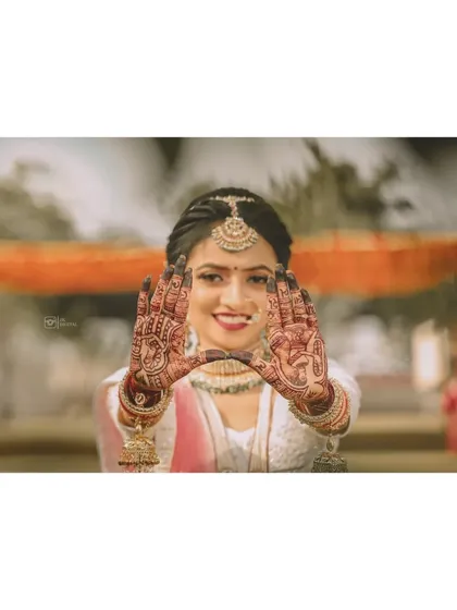 A creative bridal portrait where the bride frames her smiling face with her beautifully decorated hands, showcasing her intricate mehendi design.