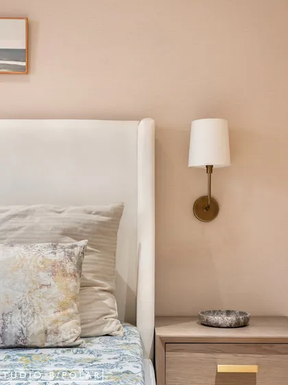 A close-up of the bedside shows the simple elegance of the design, with a classic wall-mounted lamp and a clean-lined nightstand. The textured wallpaper adds a layer of warmth.